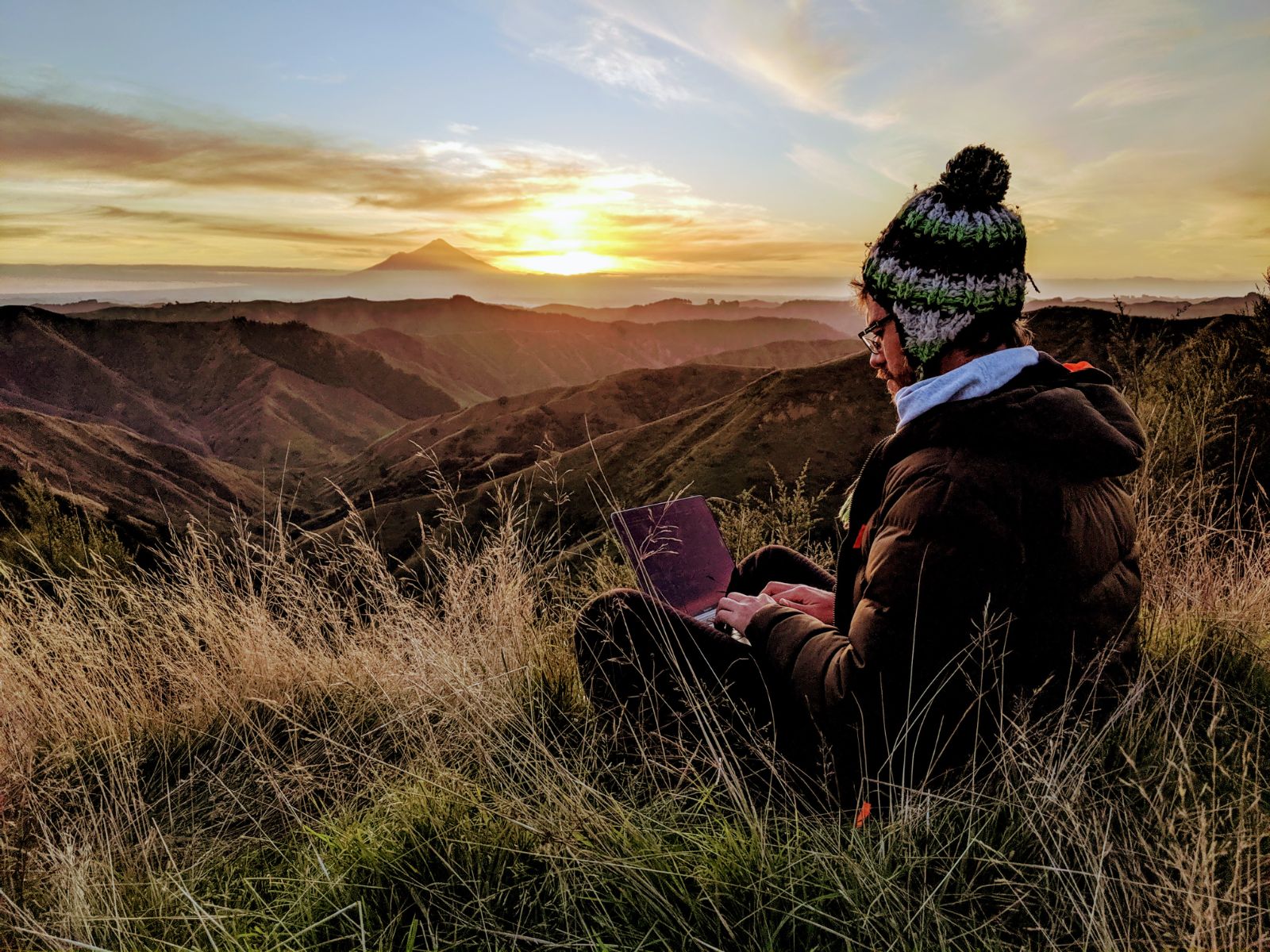 Ranger with a laptop on a hilltop at sunset in Eastern Taranaki